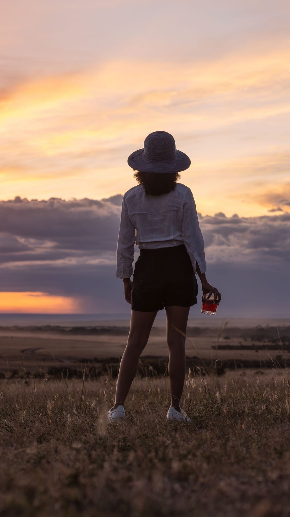 Guest in a wide-brimmed hat standing on the grassy plains watching the sunset near JW Marriott Masai Mara Lodge