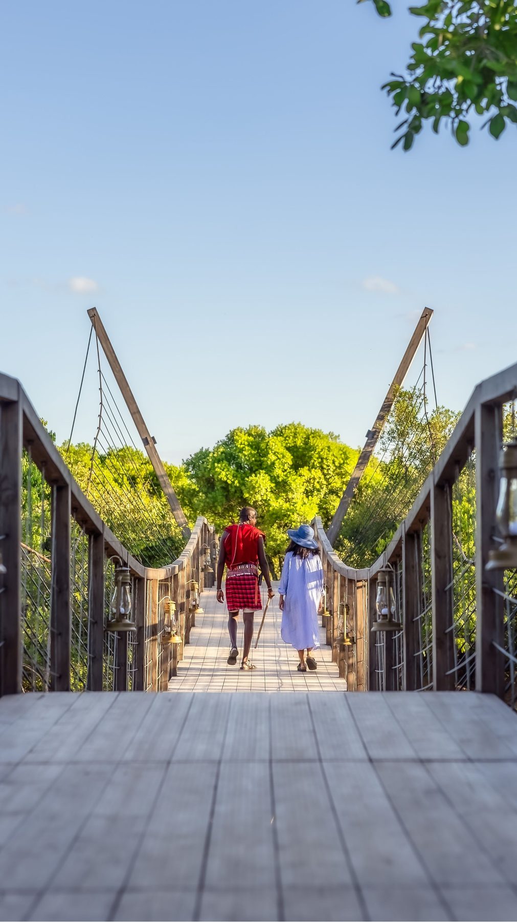 Two guests crossing a wooden suspension bridge over the treetops at JW Marriott Masai Mara Lodge