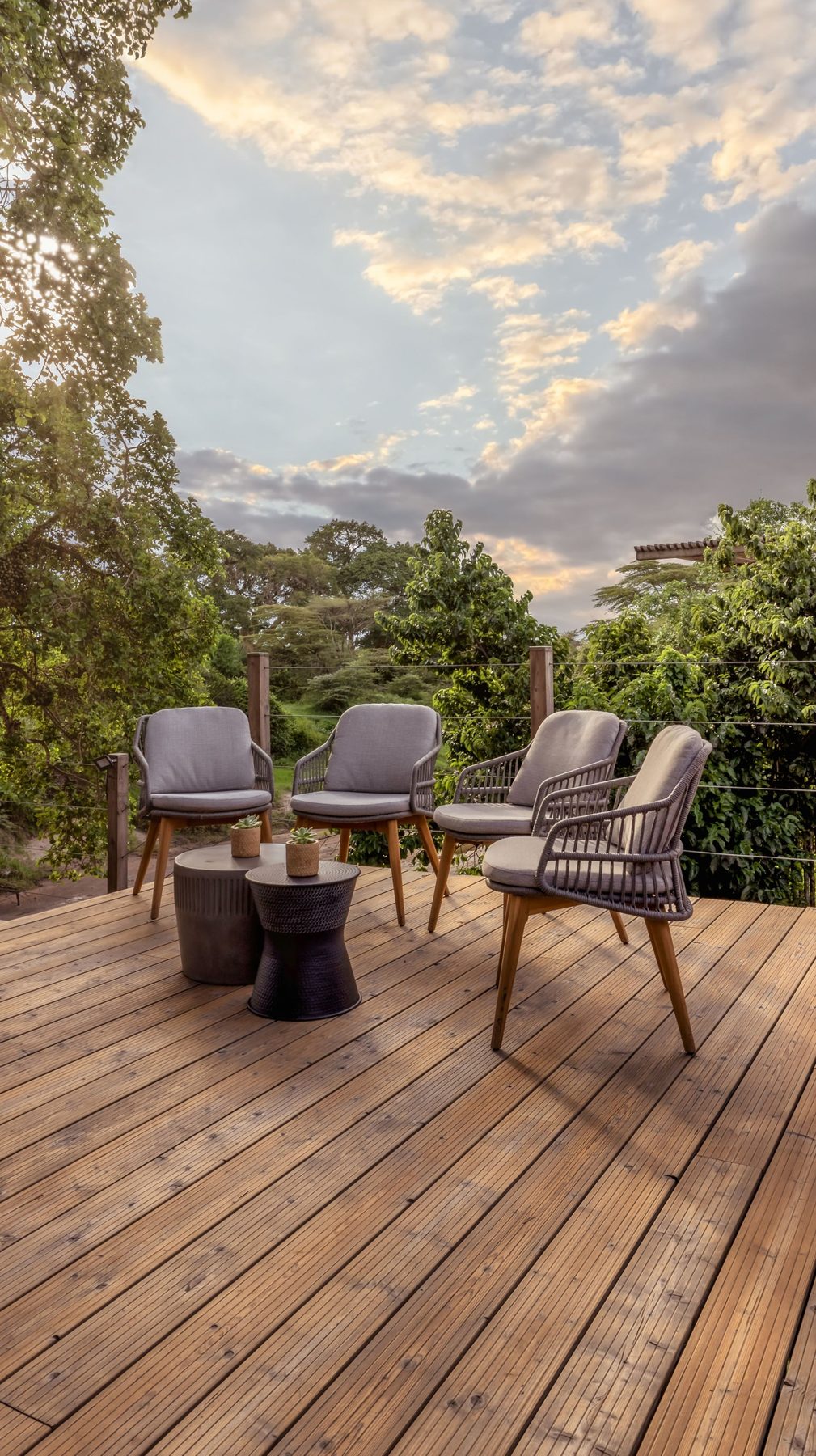 Wooden deck with armchairs and a small table looking out over the trees at JW Marriott Masai Mara Lodge
