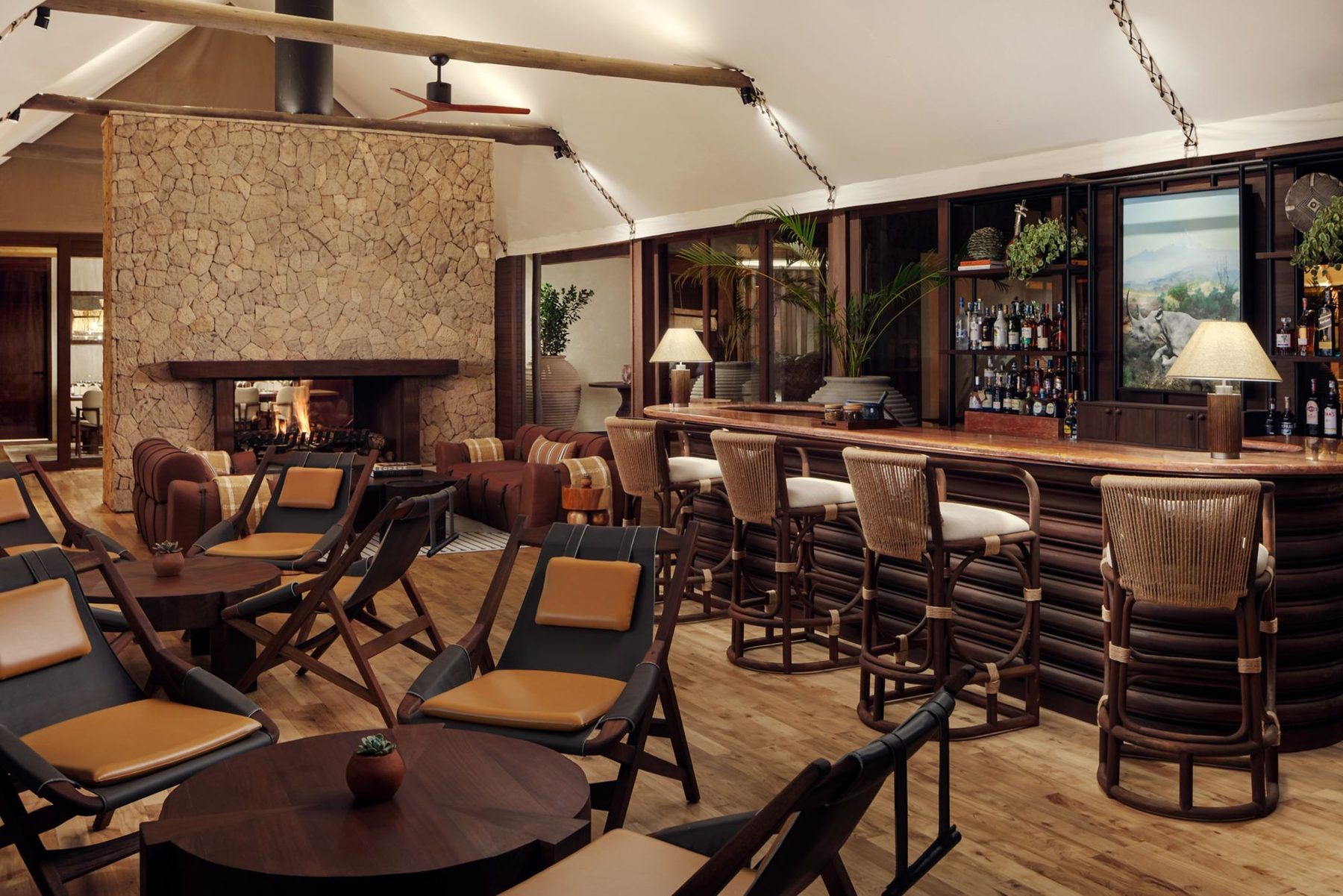 Bar with leather stools and a stone fireplace at JW Marriott Mount Kenya Rhino Reserve Safari Camp, opening onto the bush