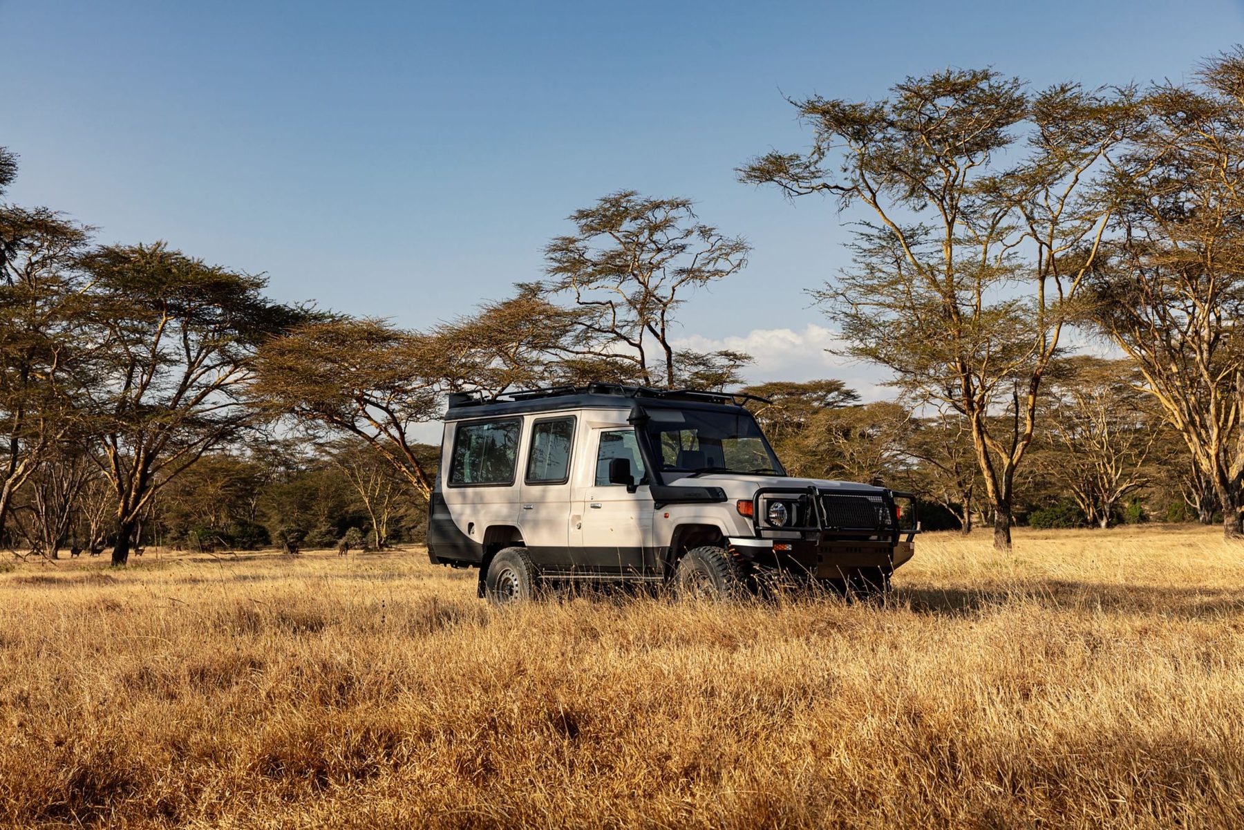 White game drive vehicle parked in golden grass among acacia trees near JW Marriott Mount Kenya Rhino Reserve Safari Camp