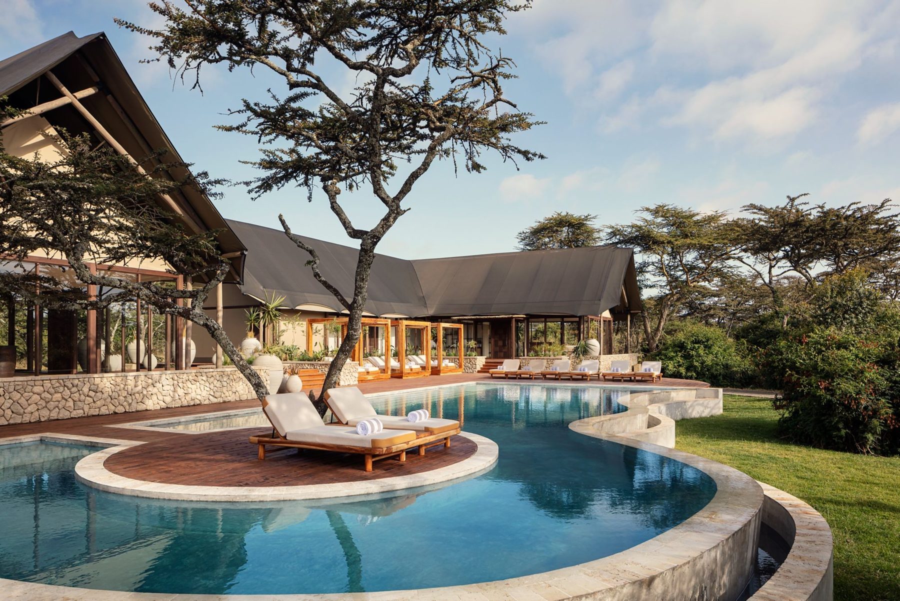 Curving swimming pool with a tree-shaded island and loungers at JW Marriott Mount Kenya Rhino Reserve Safari Camp