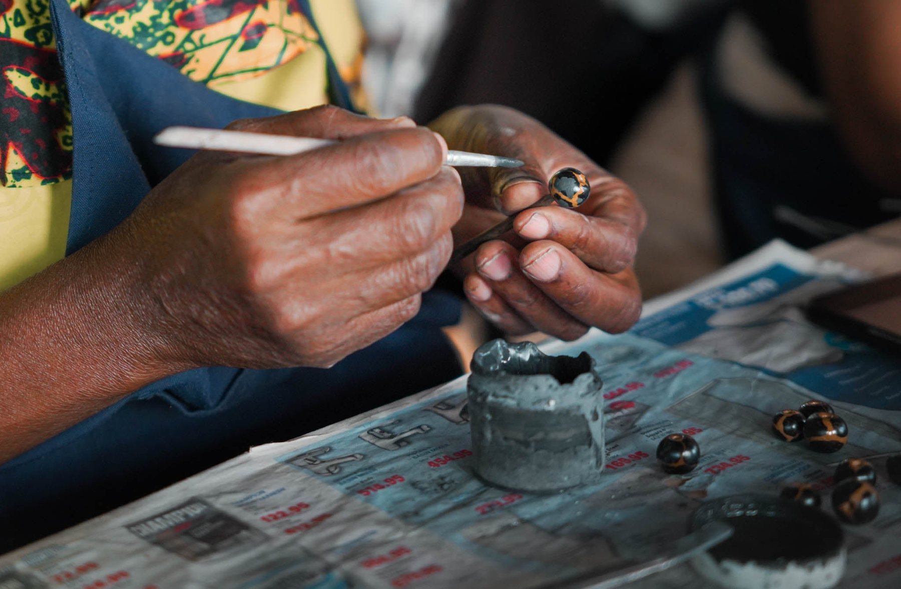 Close-up of hands painting glaze onto handmade ceramic beads at Kazuri
