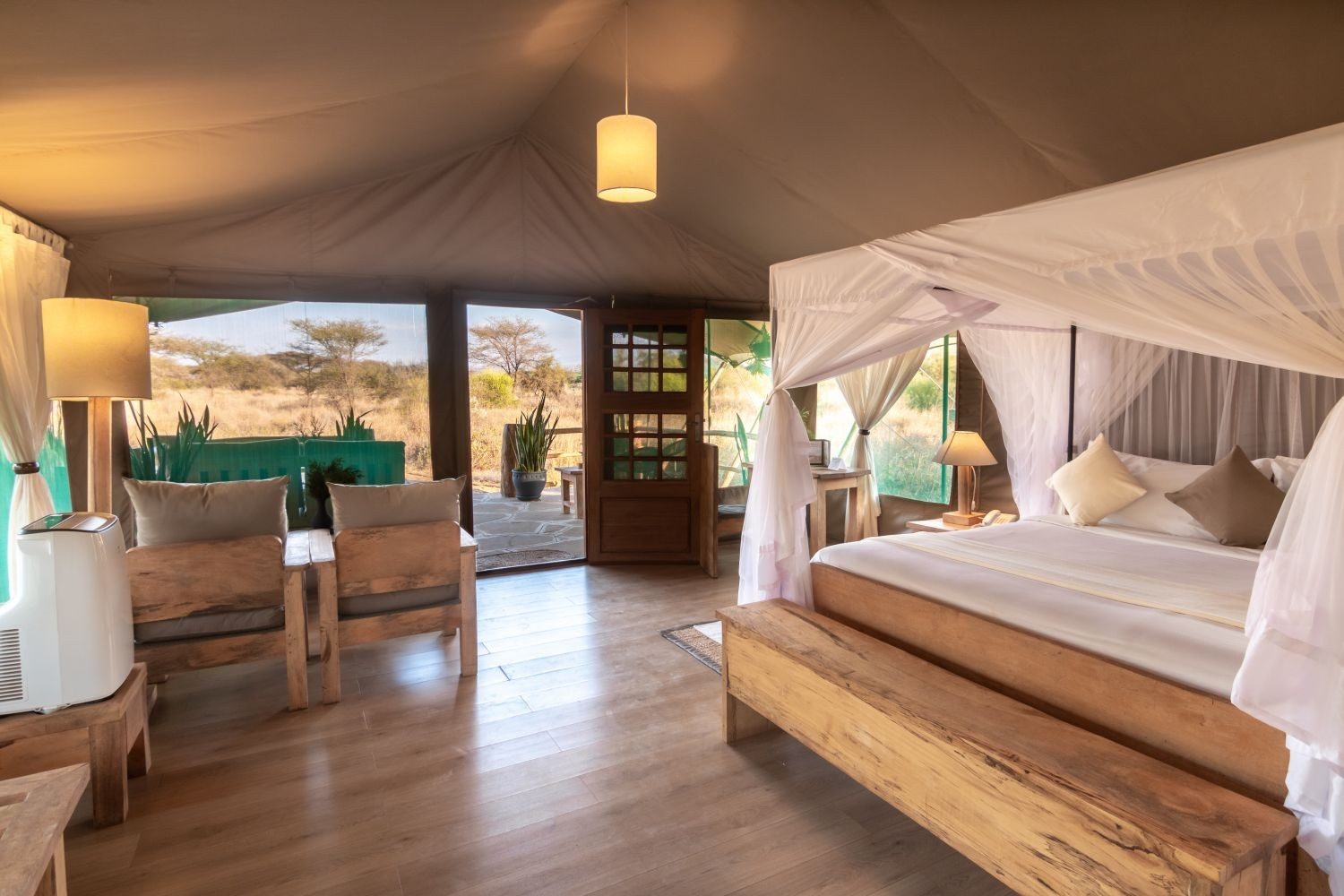 Tent at Kibo Safari Camp with a netted canopy bed, wooden floor, armchairs and a door through to the bathroom
