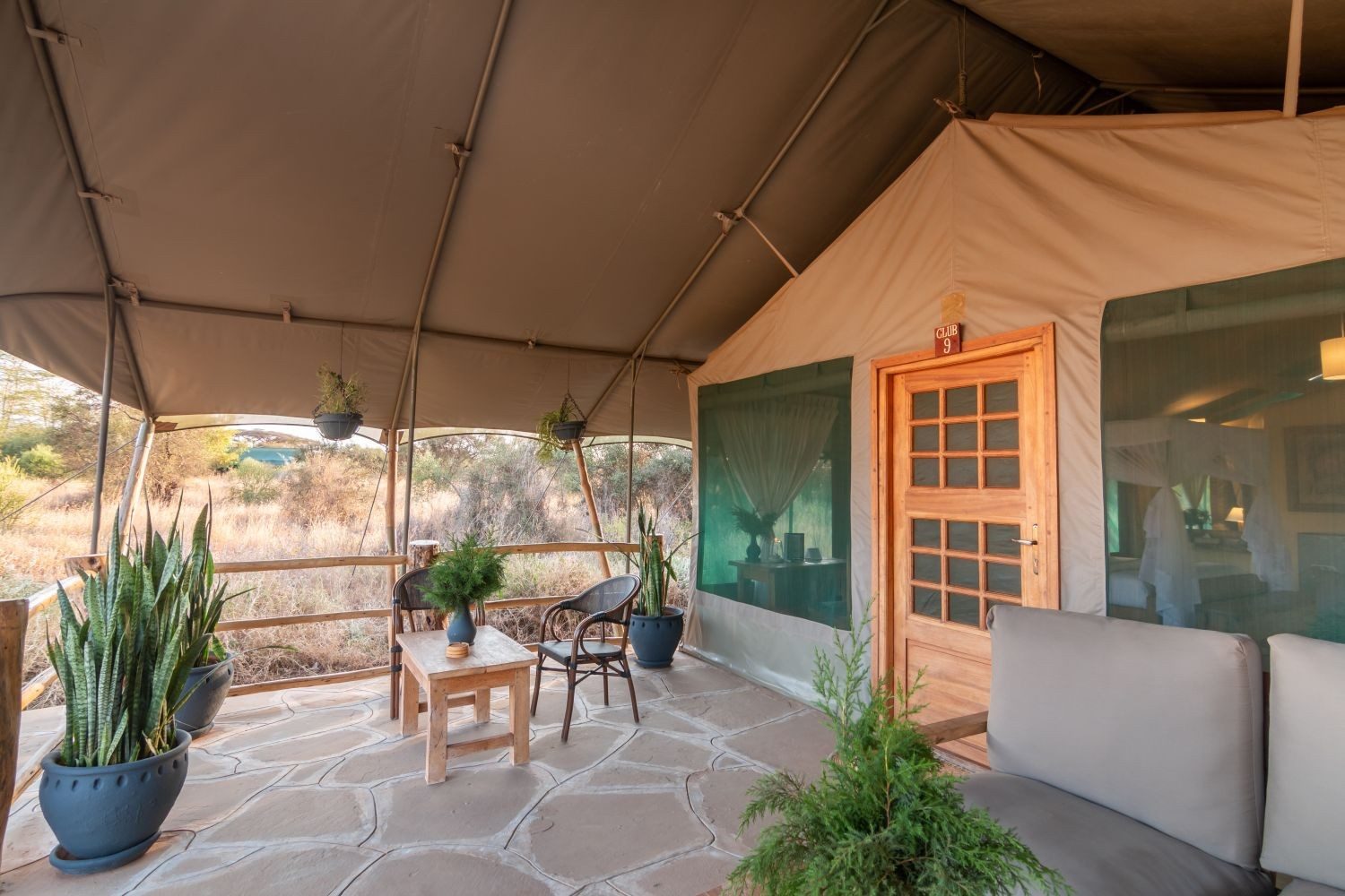 Covered veranda of a tent at Kibo Safari Camp with a stone floor, potted plants, a sofa and a small table