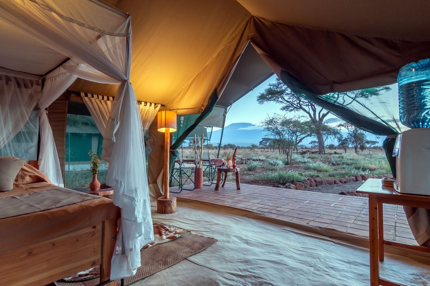 Open tent front at Kibo Safari Camp, from a netted bed out to a tiled veranda, acacias and Kilimanjaro at dusk