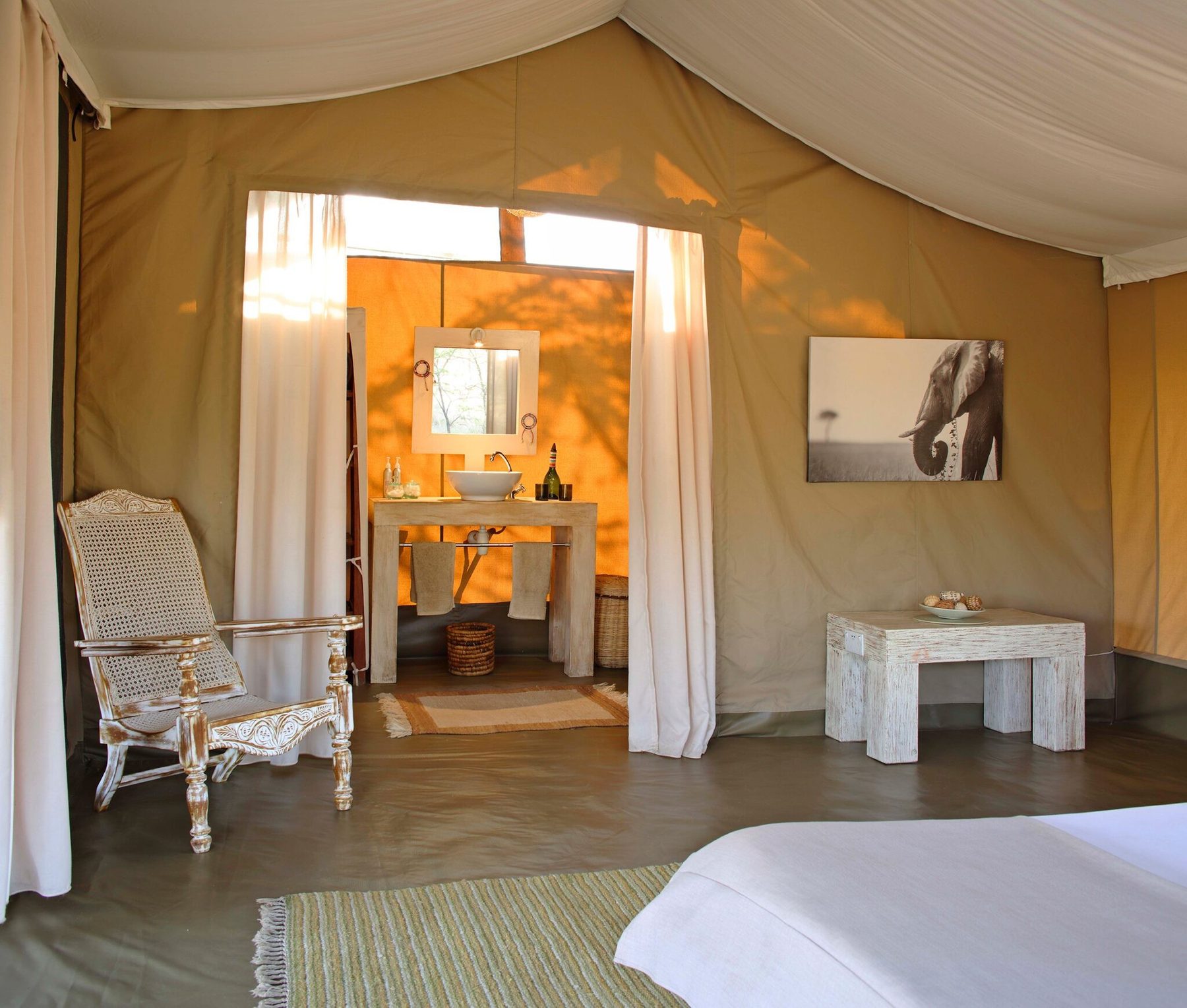 View through a tent at Kicheche Bush Olare to the bathroom, with a washstand, mirror and white curtains