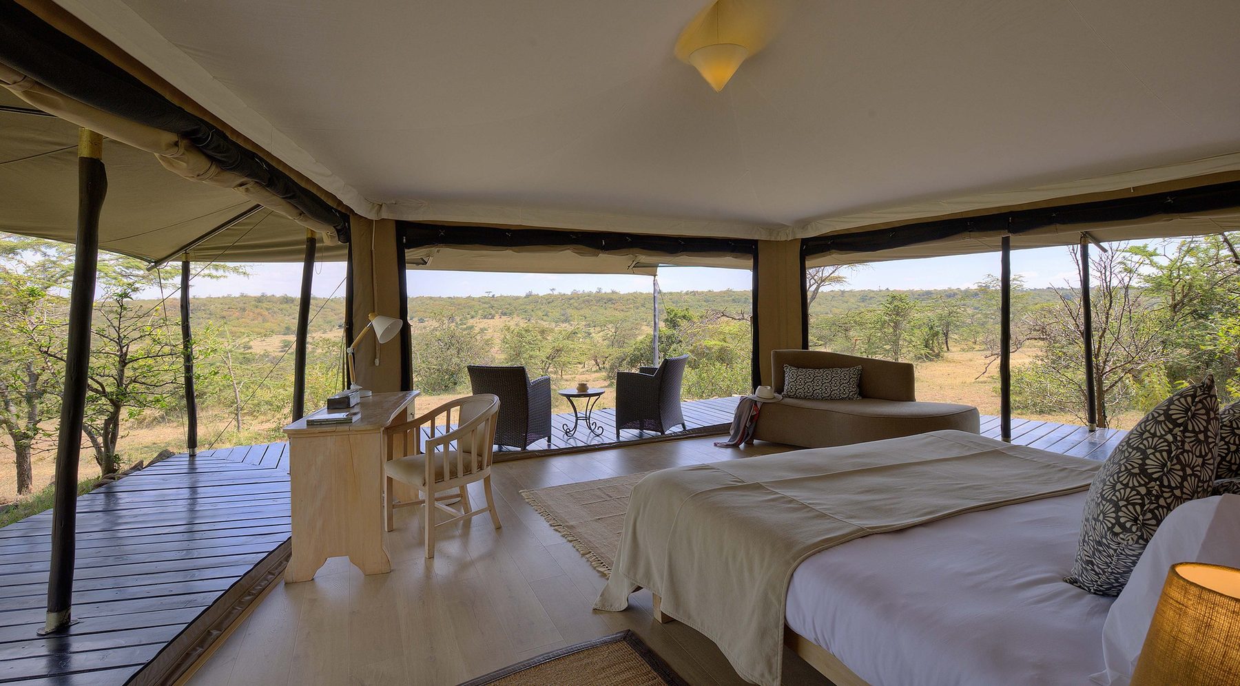 Bed and seating area inside a tent at Kicheche Bush Olare, with screened sides open to a deck and acacia trees