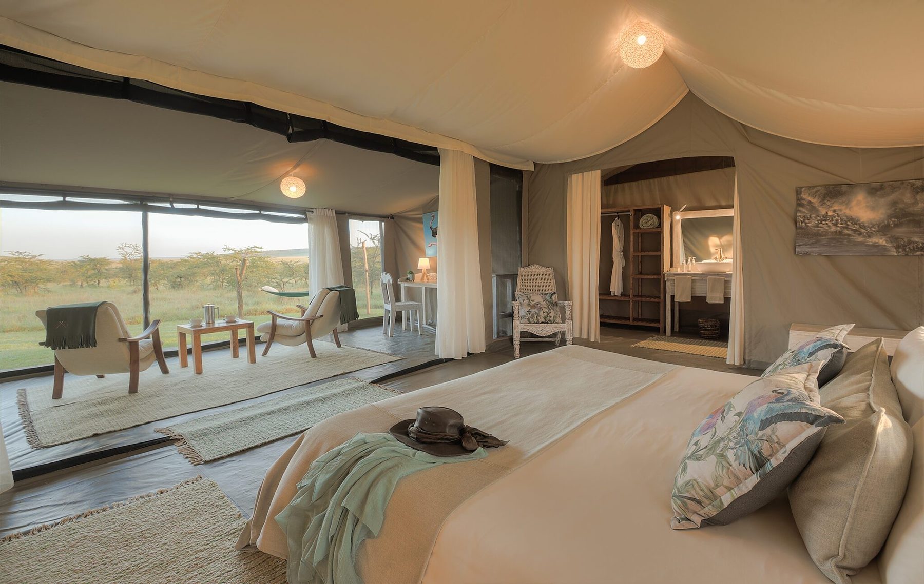 Softly lit tent at Kicheche Bush Olare with a bed, armchairs and a doorway through to the bathroom