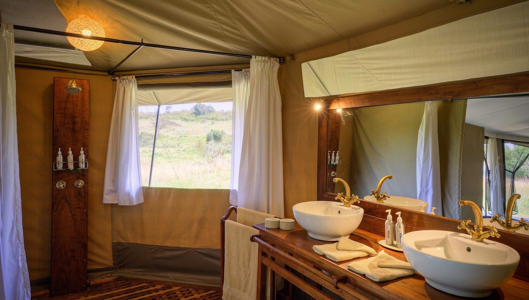 Twin basins on a wooden vanity in a tent bathroom at Kicheche Mara North, with windows onto bush