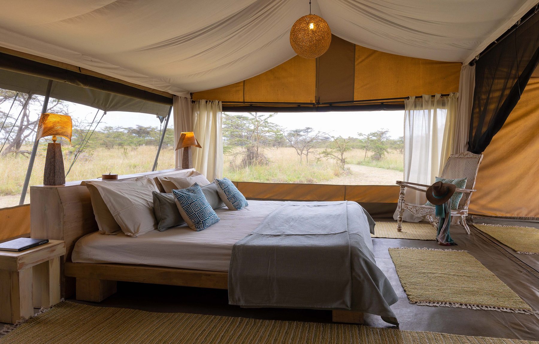 Double bed with blue cushions in a tent at Kicheche Mara North, wide windows looking out to grassland
