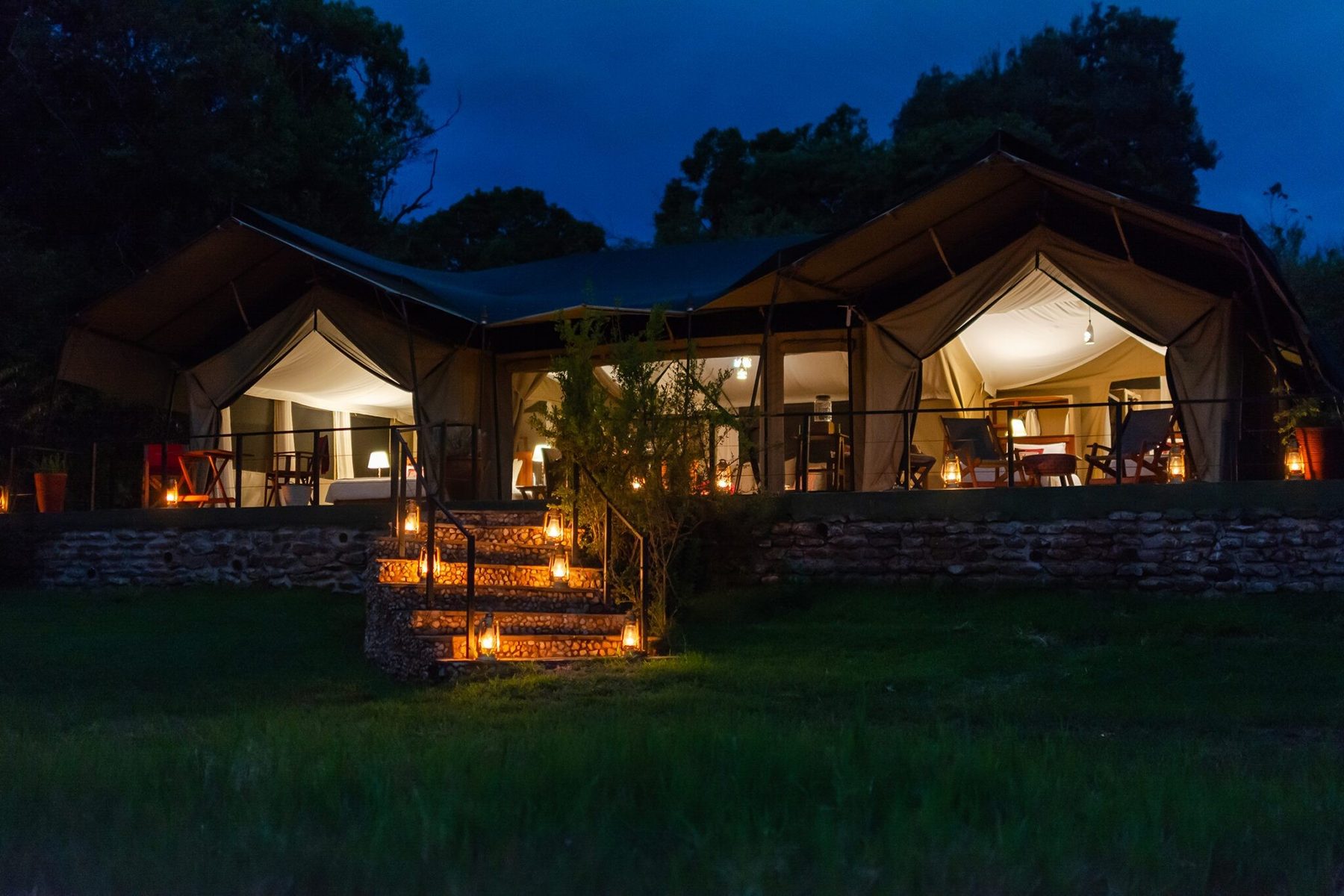 Tents at Kicheche Mara North glowing with lamplight at night, a lantern-lined path leading up from the lawn