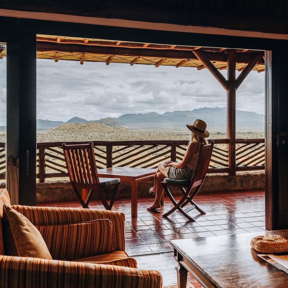 Guest relaxing on a room balcony at Kilaguni Serena Safari Lodge, looking out over bush and distant hills