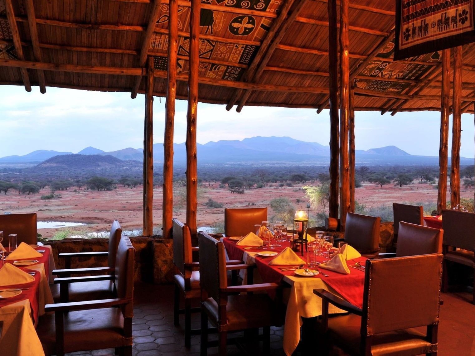 Dining tables set with orange cloths under a timber roof at Kilaguni Serena Safari Lodge, overlooking the plains and hills