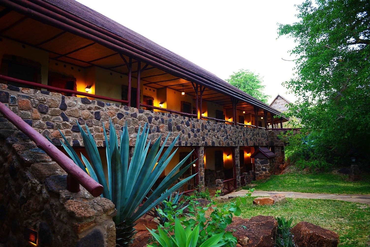Stone guest wing with wooden balconies above a garden of agave and shrubs at Kilaguni Serena Safari Lodge