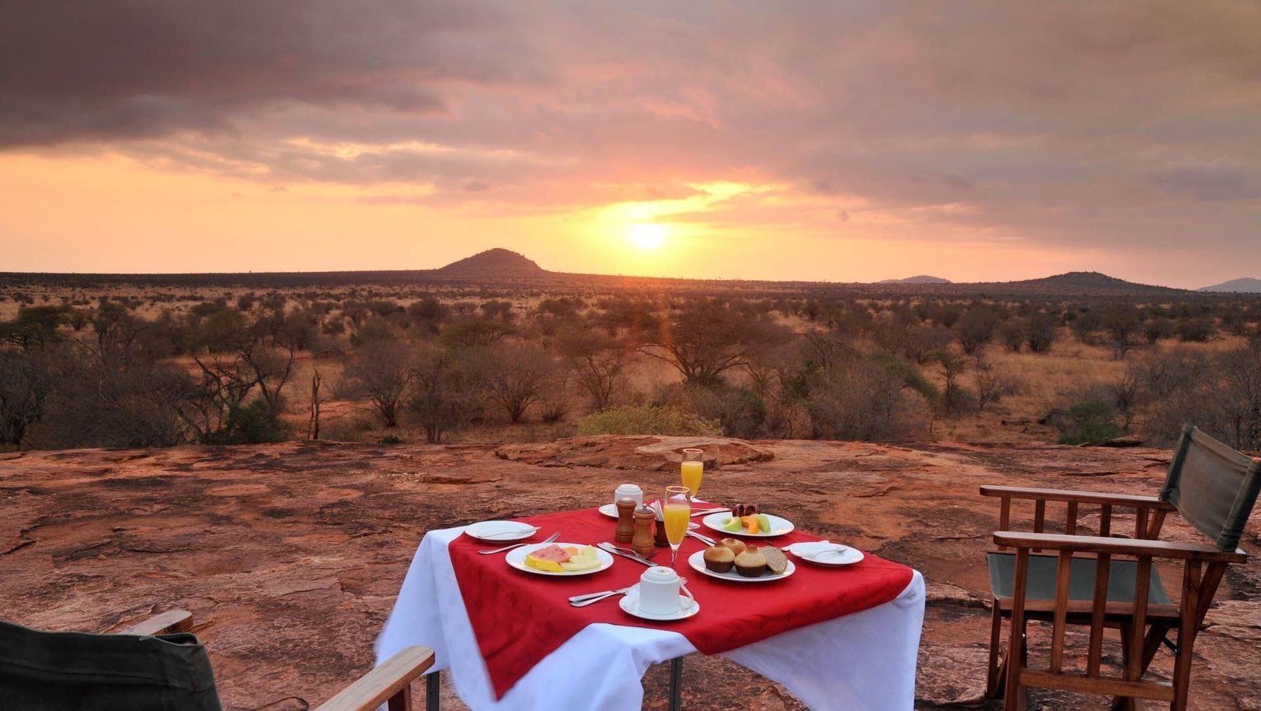 Table laid with a red cloth for dinner on open ground as the sun sets over Tsavo West