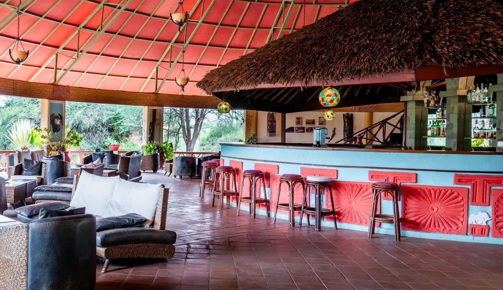Bar at Kilima Safari Camp with red stools under a thatched canopy, beside a lounge with sofas