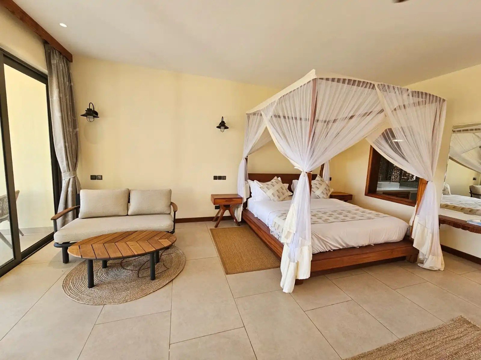 Bright bedroom at Kilima Safari Camp with a four-poster bed draped in white netting, a sofa and a round coffee table