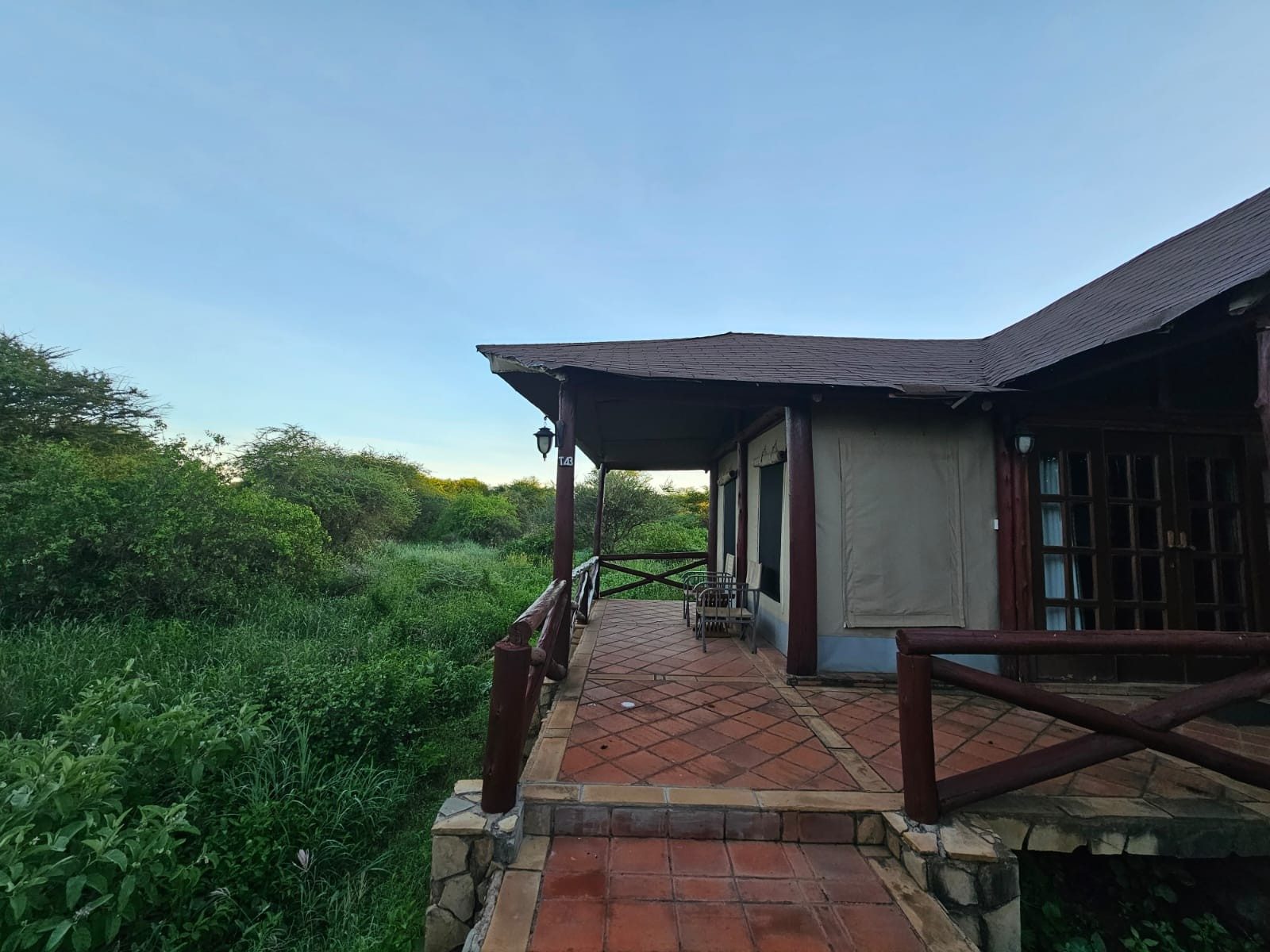 Tent with a covered brick veranda and wooden railings at Kilima Safari Camp, looking over green bush