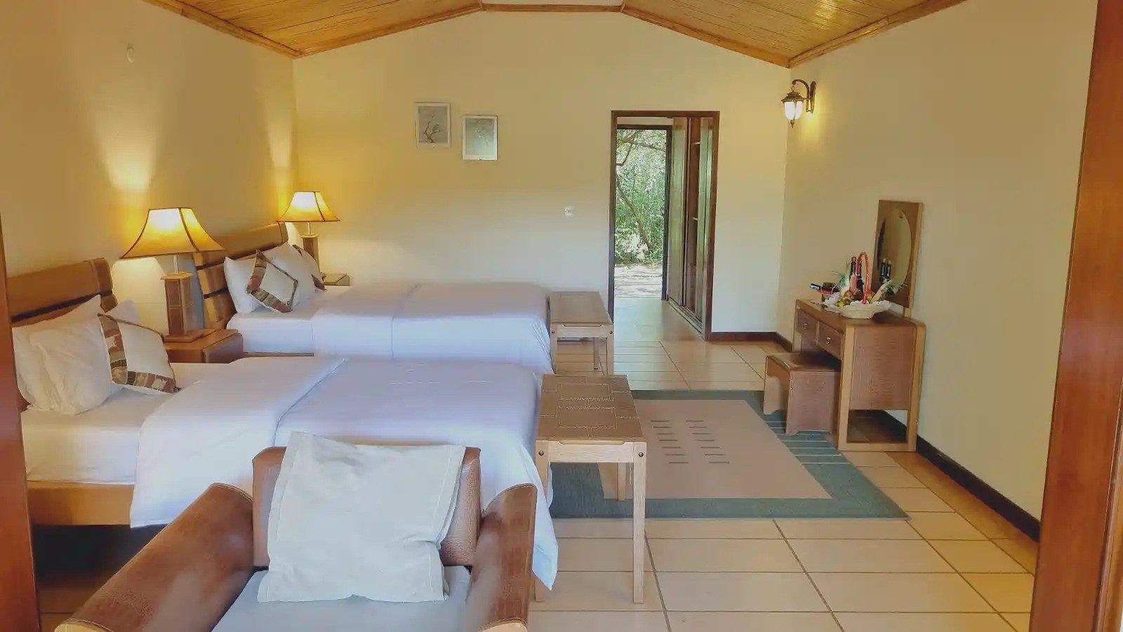 Twin room at Kilima Safari Camp with white beds, bedside lamps, a desk and a wooden ceiling