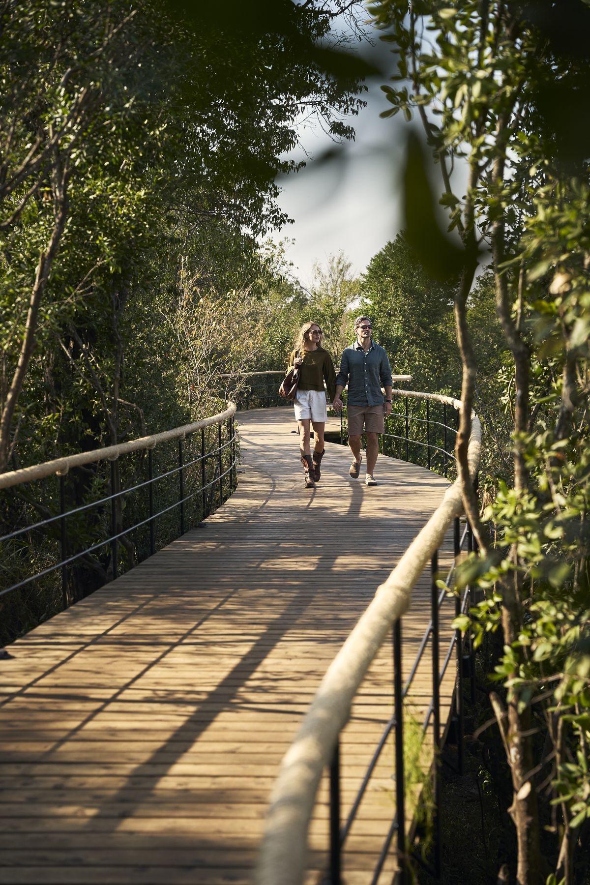 Two guests walking along a raised wooden boardwalk through trees at Kinara