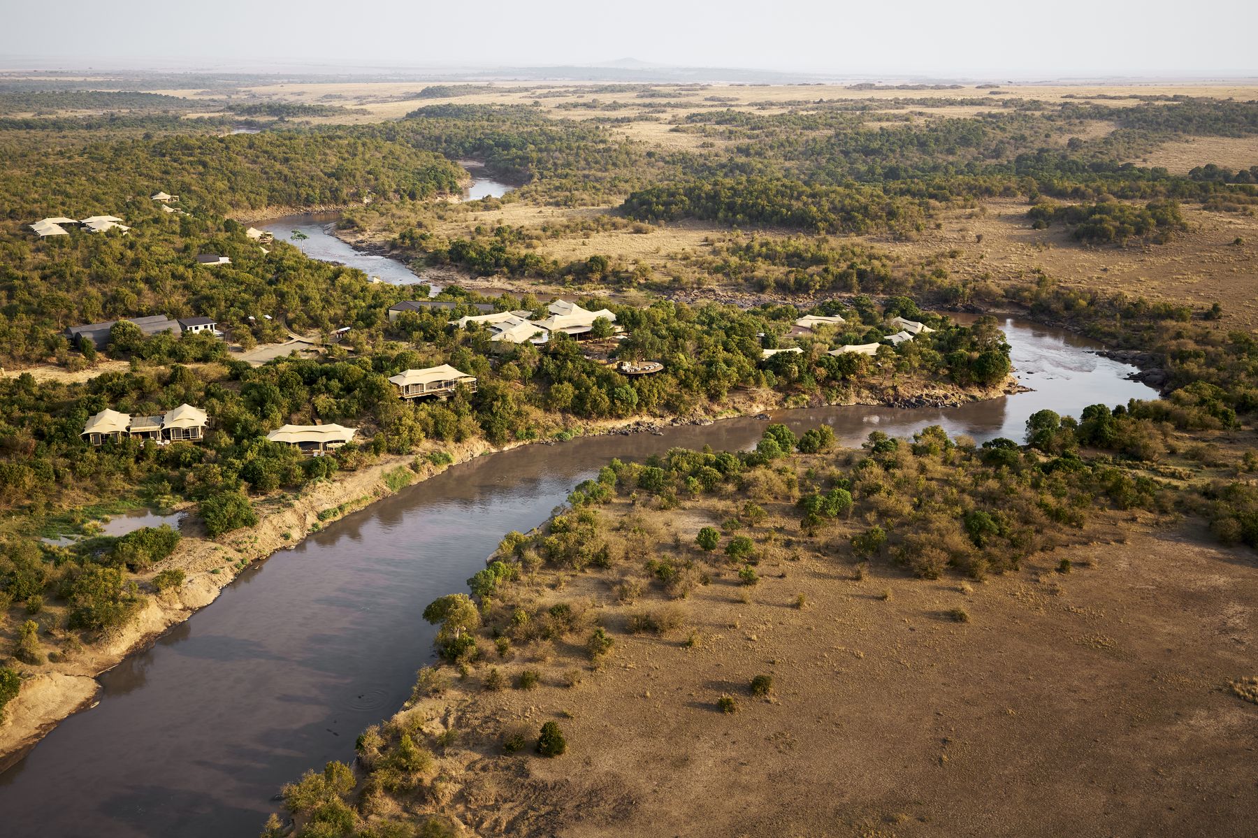 Aerial view of Kinara’s tents among trees along a bend of the Mara River, with open plains beyond