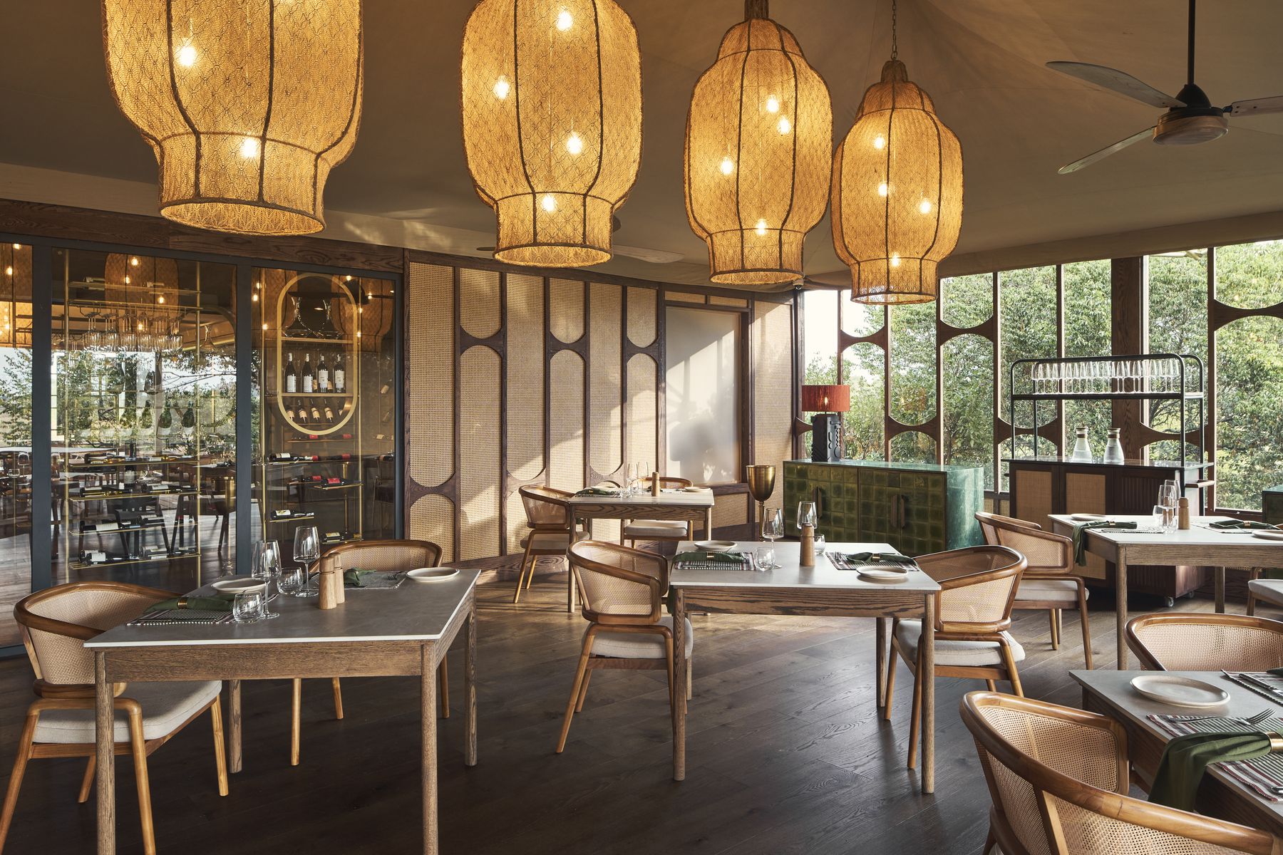 Asili, Kinara’s restaurant, with woven lanterns over set tables and windows onto the trees