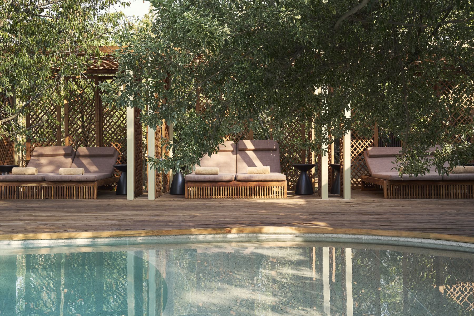 Day beds under shade on the deck beside Kinara’s pool, with trees overhead