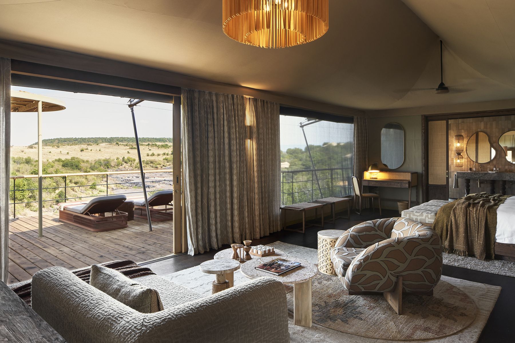 Tented suite at Kinara with sofas and armchairs, glass doors open onto a deck above the river and the plains