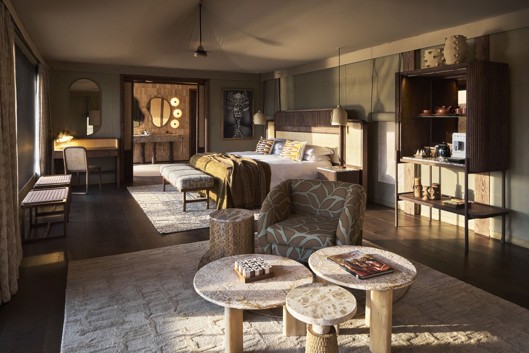 Bedroom in a Kinara suite with a large bed, woven rugs, a reading chair and a small bar cabinet