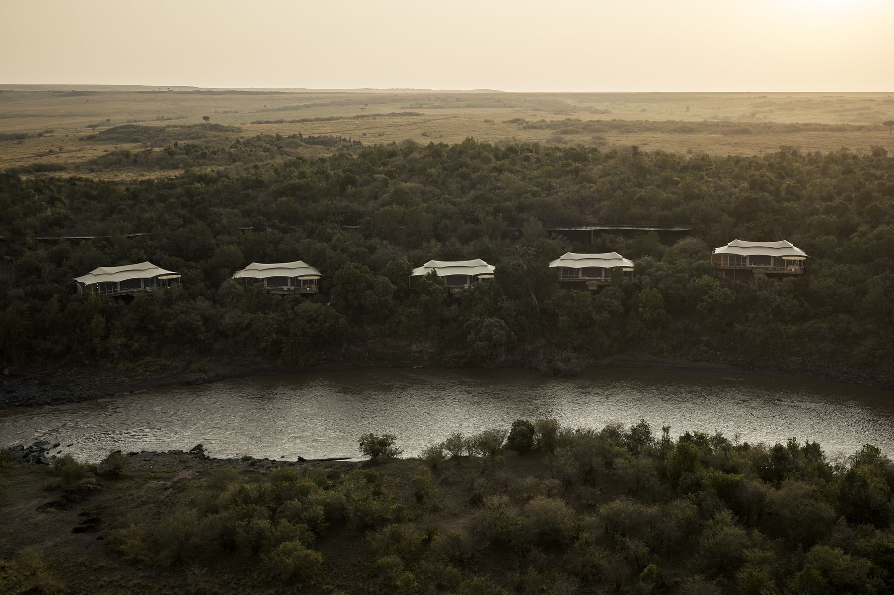 A row of Kinara’s suites above the trees and the river in early morning light