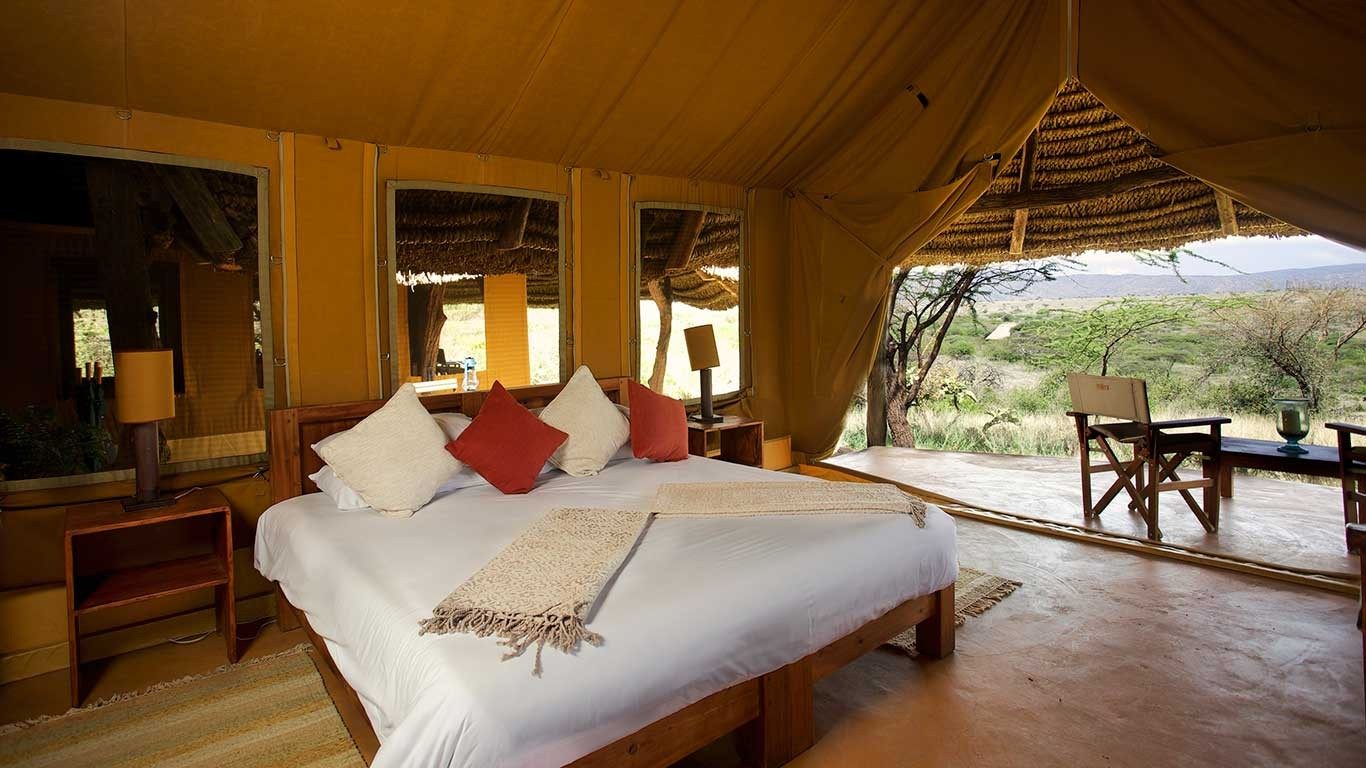 Tent at Elewana Lewa Safari Camp with a double bed, red cushions and an open front onto a veranda with chairs