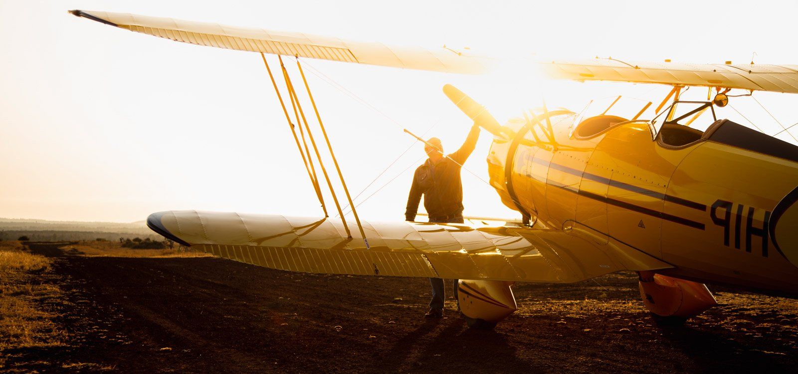 A pilot beside a vintage yellow biplane on the Lewa airstrip, backlit by the low sun