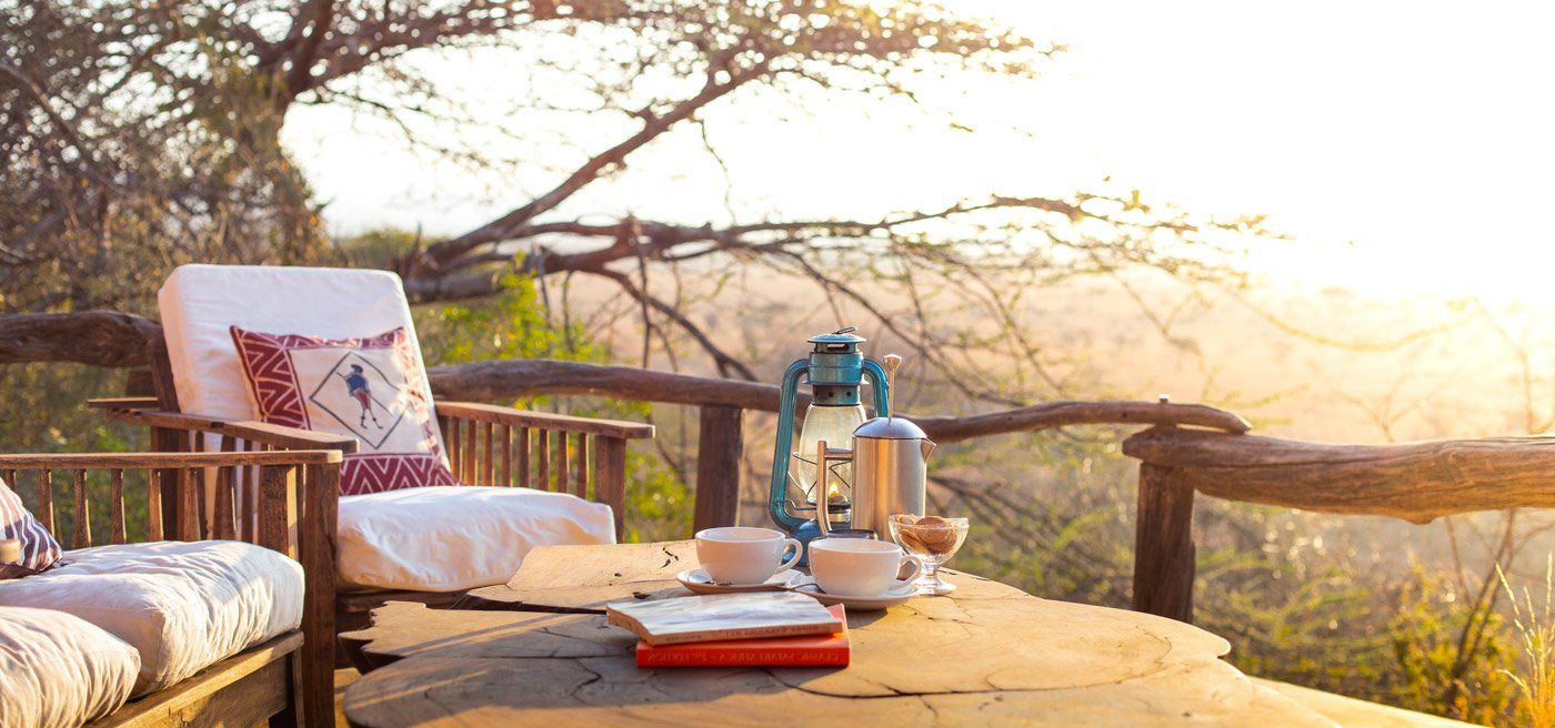 Cushioned chairs, a hurricane lamp and coffee on a wooden deck at Lewa Wilderness, overlooking the plains at sunrise
