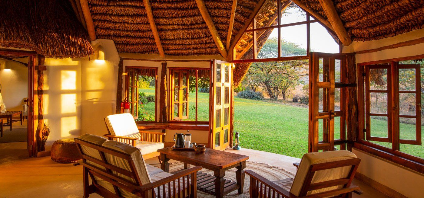 Sitting room of a garden cottage at Lewa Wilderness under a thatched roof, with armchairs and windows onto the lawn