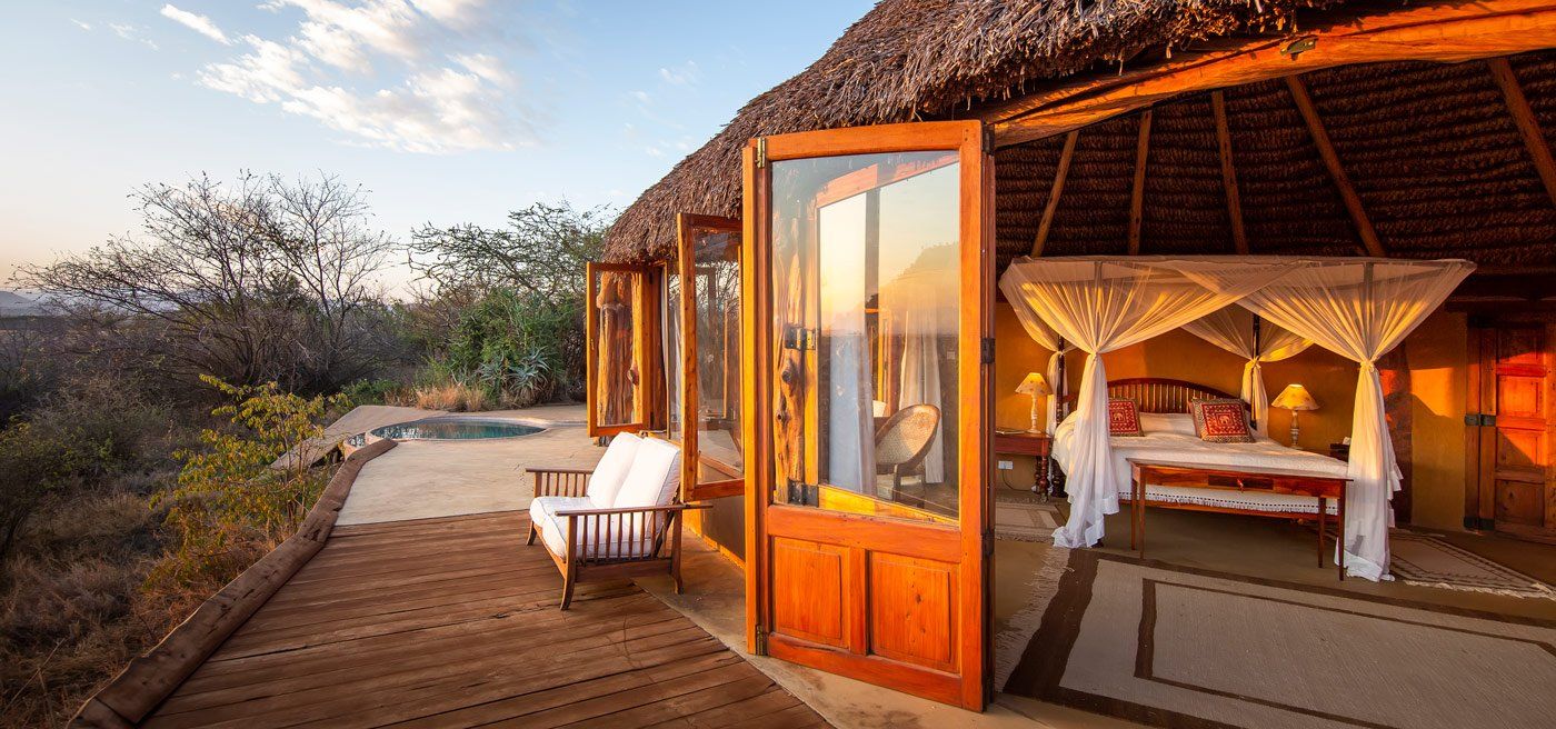 Cottage at Lewa Wilderness with a four-poster bed and tall wooden doors open onto a deck, with a small pool beside it