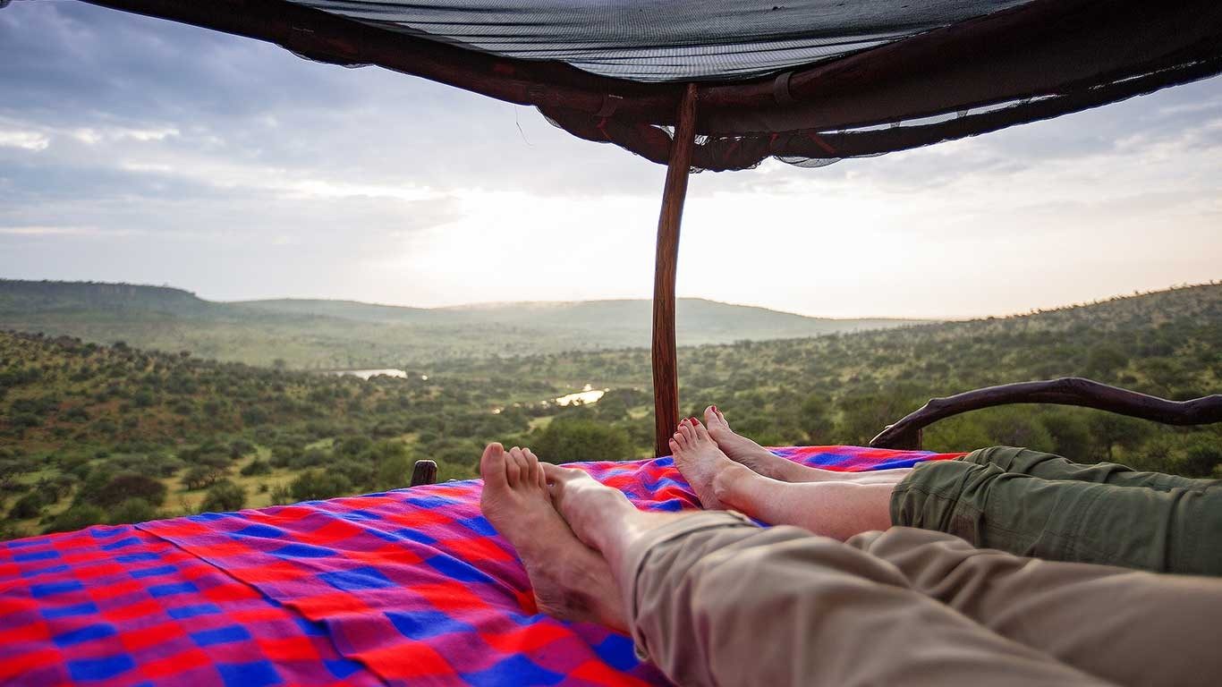 Guest stretched out on a star bed at Loisaba Star Beds, looking out over a green river valley