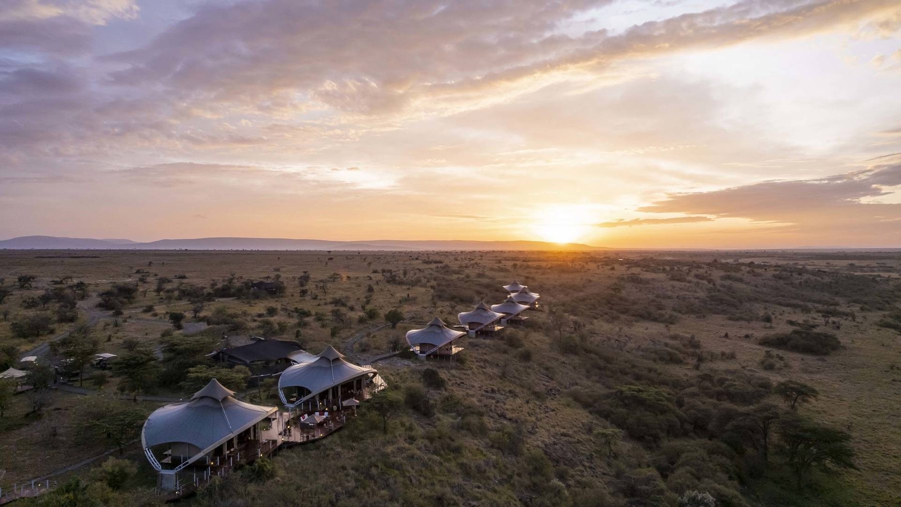 Aerial view of Mahali Mzuri’s curved-roof tents strung along a ridge above the plains at sunset