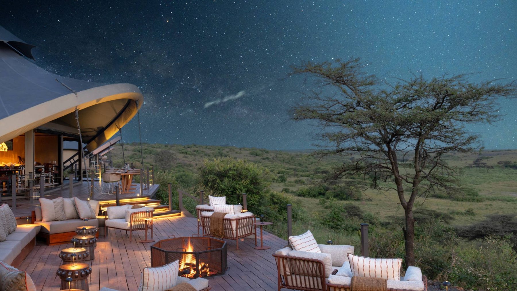 Main deck at Mahali Mzuri lit by lanterns and a fire under a starry sky, sofas facing the dark plains