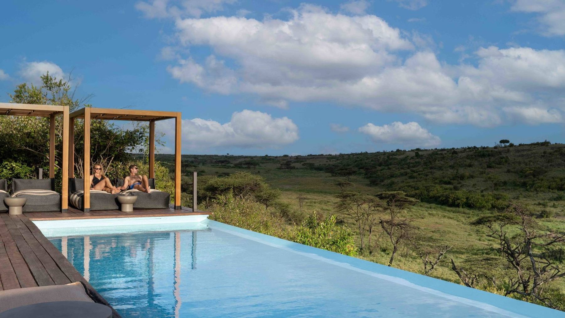 Infinity pool with shaded daybeds at Mahali Mzuri, looking over a green valley of trees and bush