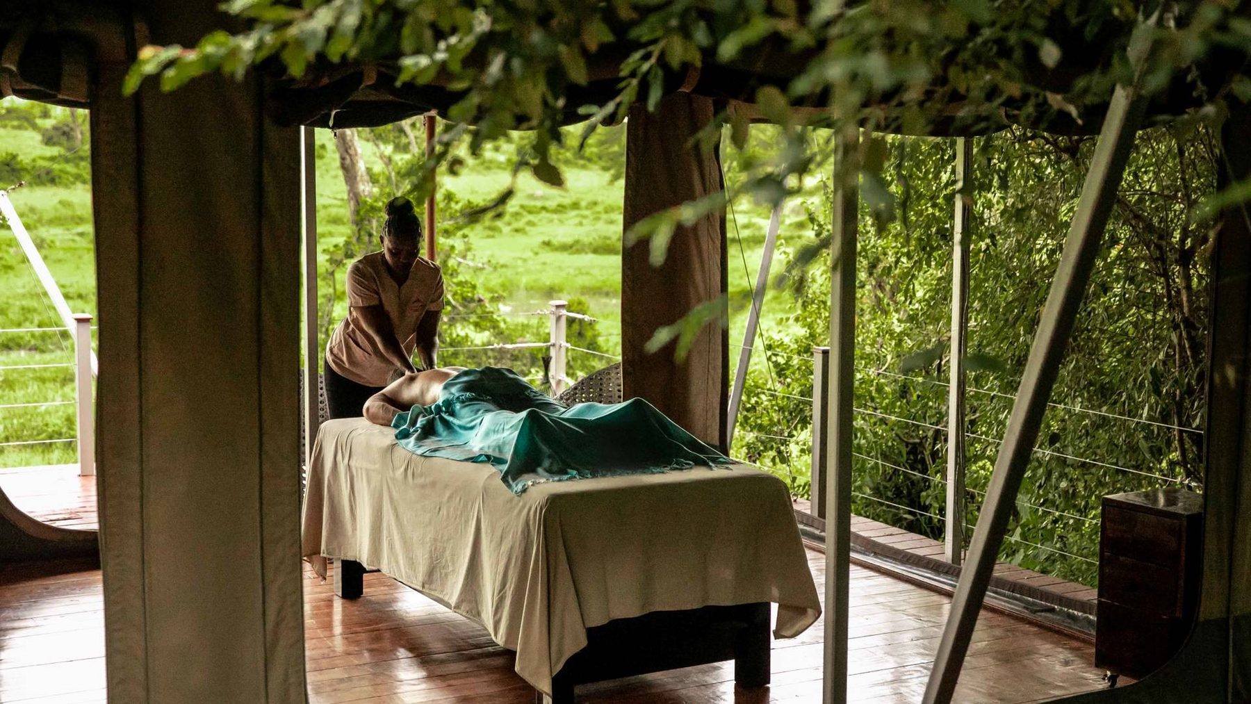 Guest receiving a massage on a table in an open-sided treatment room among leafy trees at Mahali Mzuri