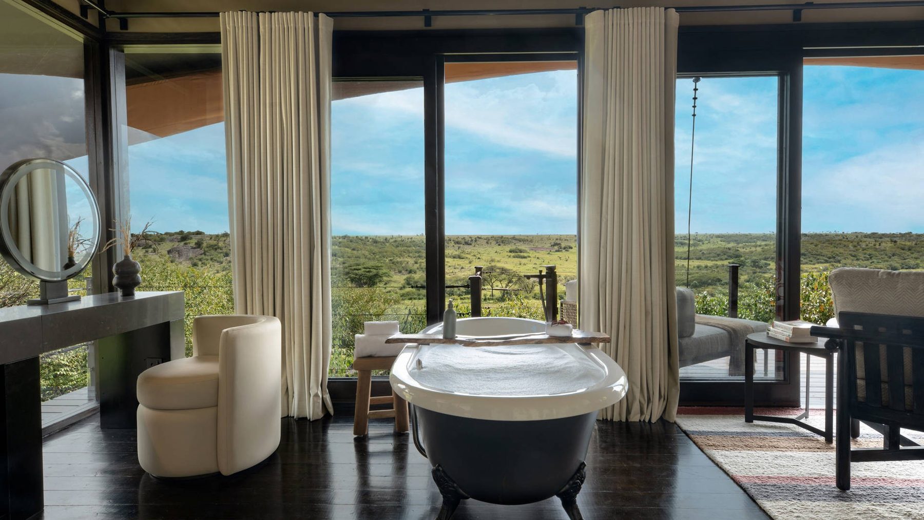 Freestanding bathtub by tall windows in a tented suite at Mahali Mzuri, looking out over green bush