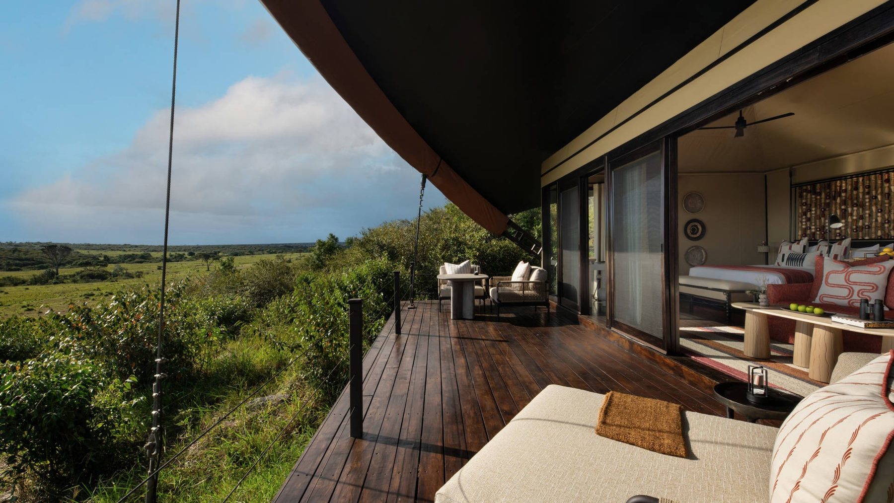 Wooden deck of a tented suite at Mahali Mzuri with a daybed, glass doors and a view over green hills