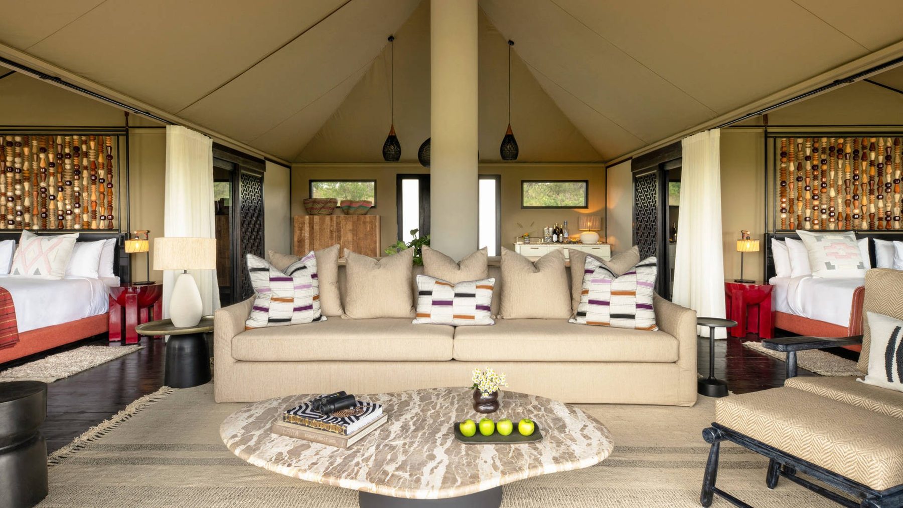 Tented suite at Mahali Mzuri with a cream sofa, marble coffee table and red armchairs beside the bed