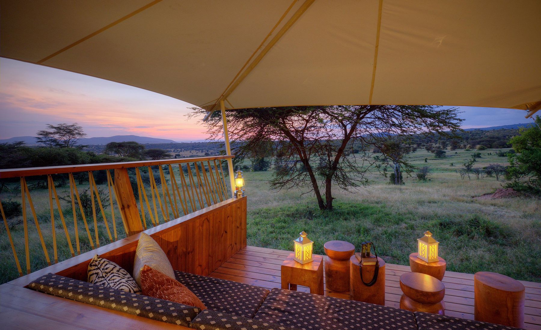 Cushioned seating and lanterns on a suite deck at Mara Bushtops at dusk, with acacias on the plains below