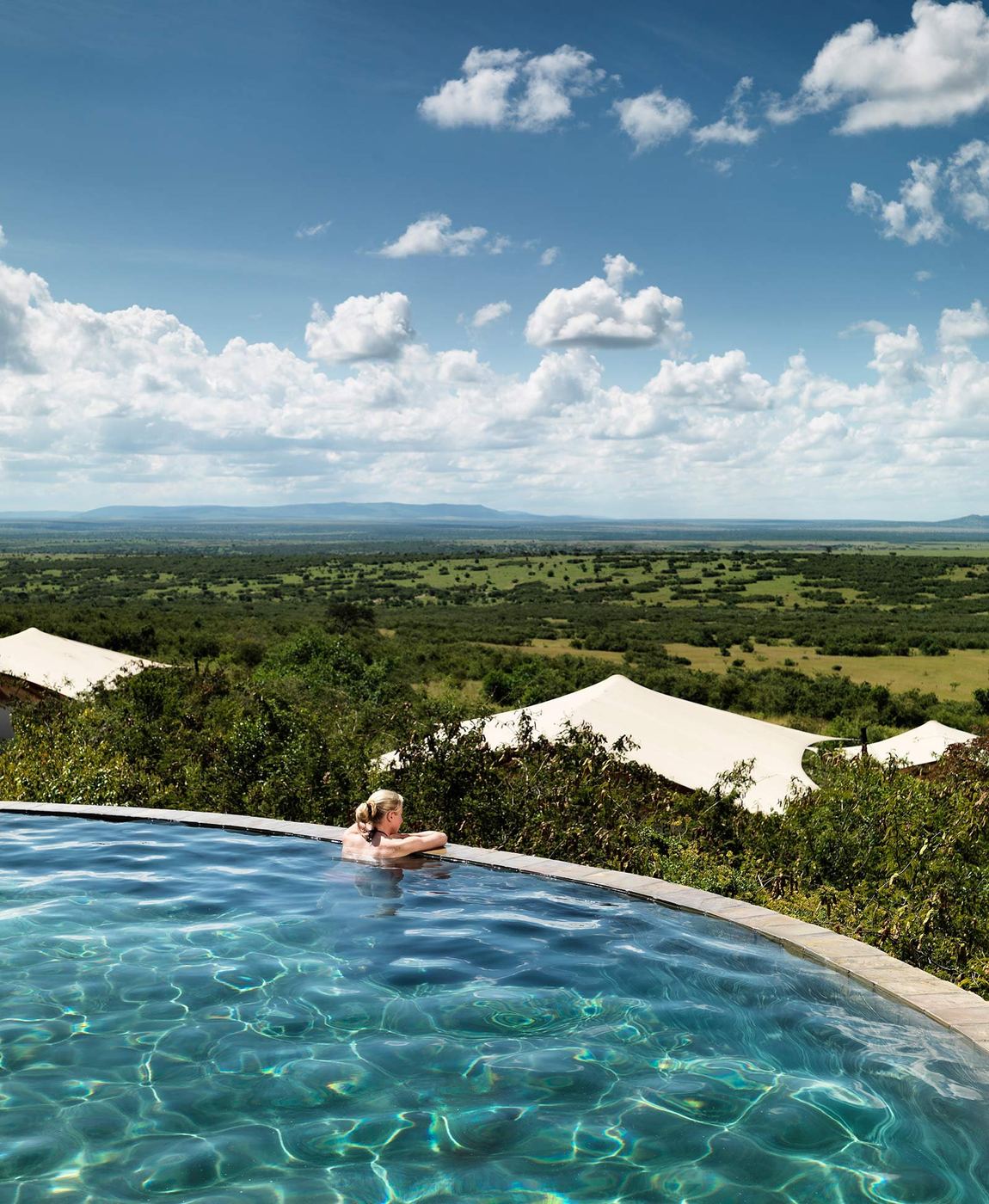 A guest resting at the edge of the infinity pool at Mara Bushtops, looking over tented roofs to the green plains