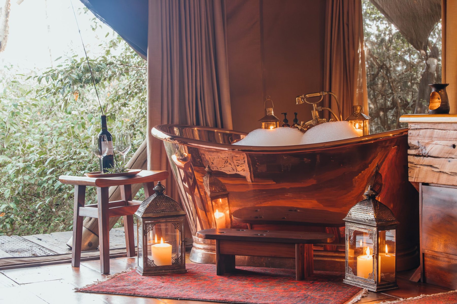 Copper bathtub lit by lanterns and candles in a tent at Mara Nyika Camp, with bush visible through the canvas