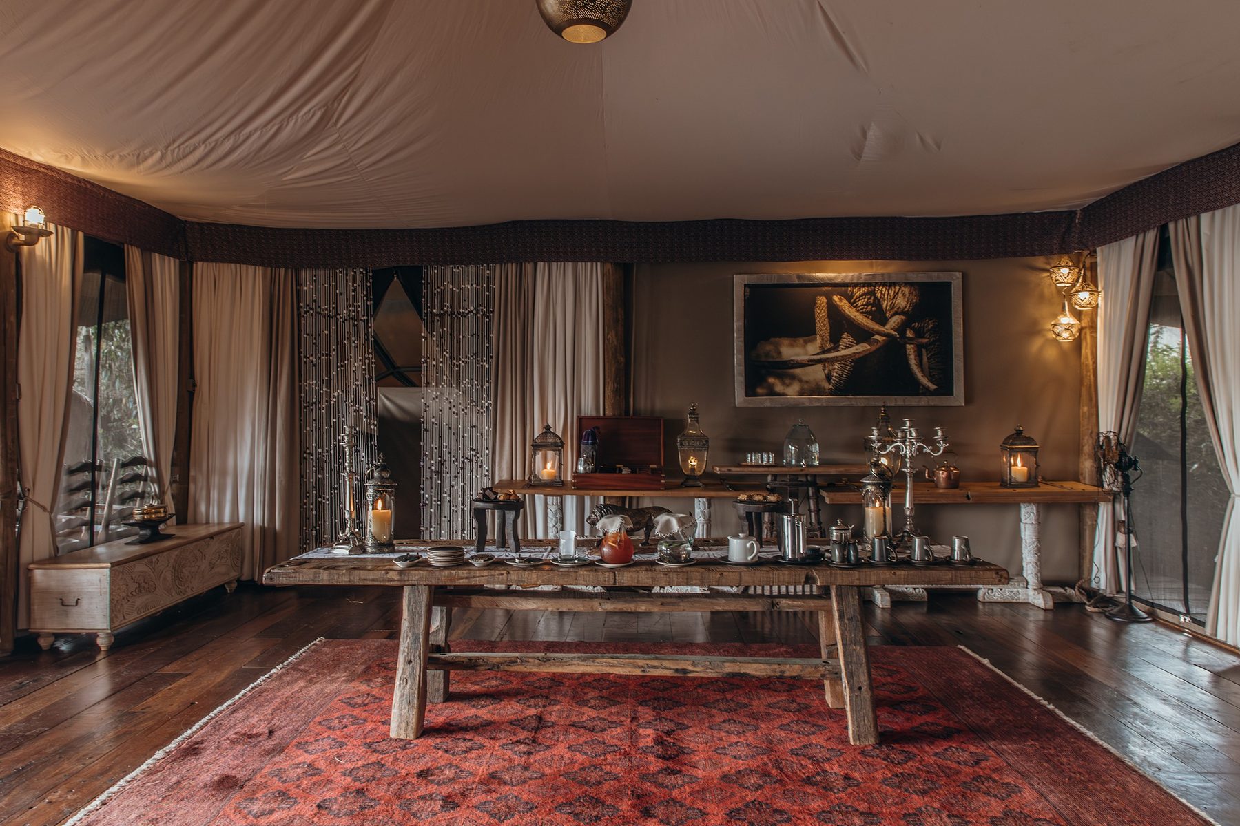 Dining tent at Mara Nyika Camp with a long wooden table, candelabras and a rug under canvas