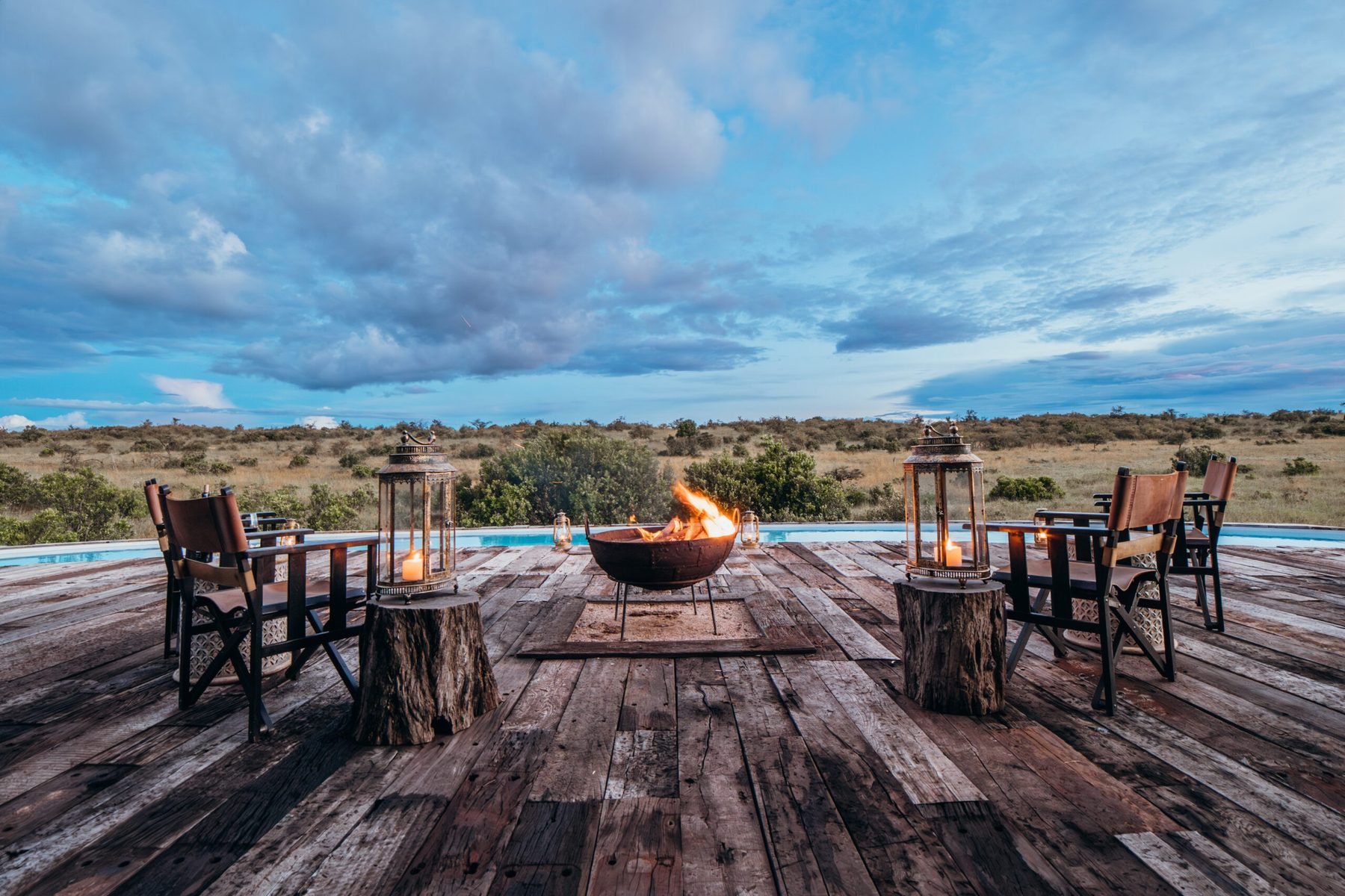 Fire bowl surrounded by lanterns and director’s chairs on a wooden deck looking out over the plains at Mara Nyika Camp
