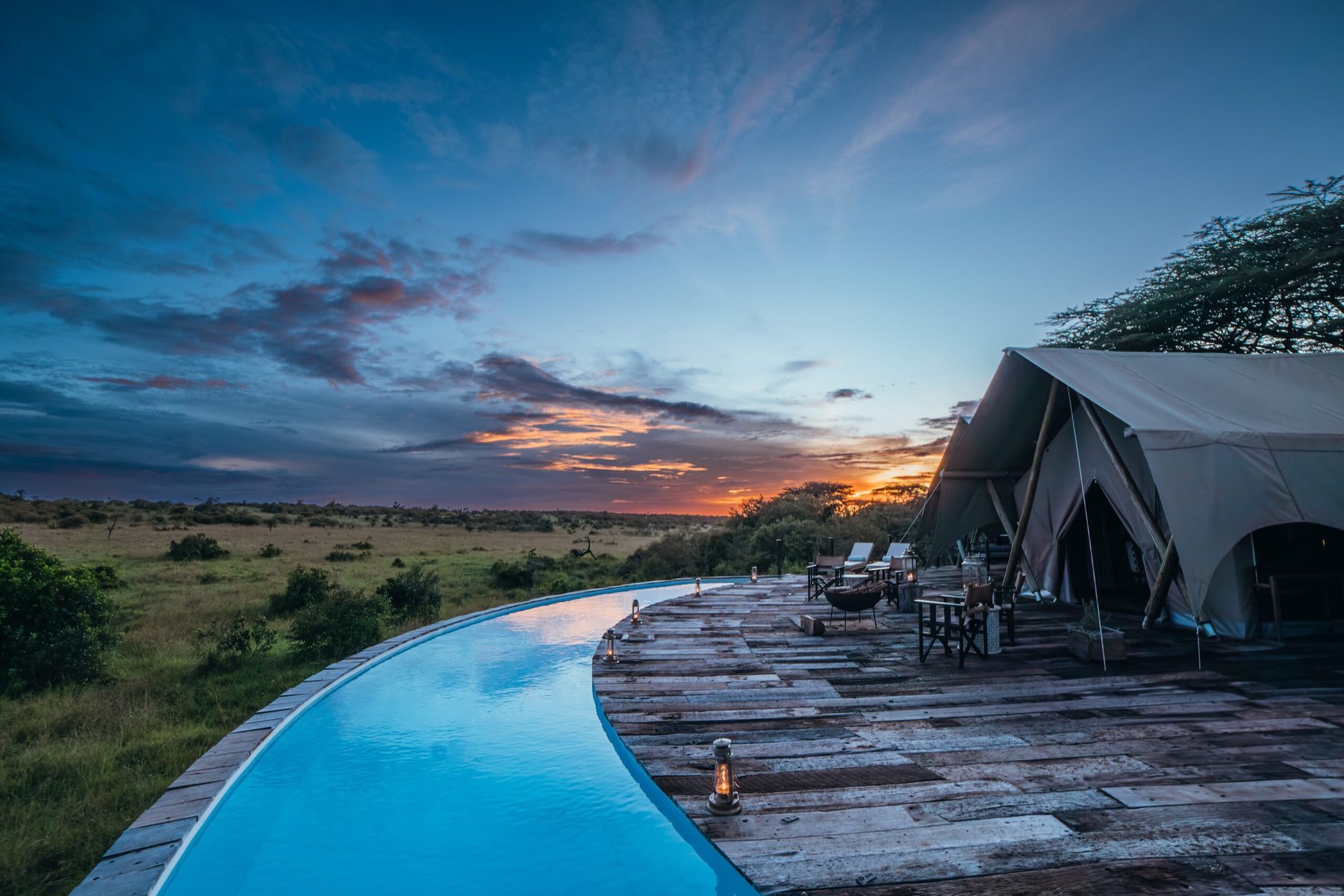 Curved swimming pool beside a wooden deck and tents at Mara Nyika Camp under a dramatic sunset sky